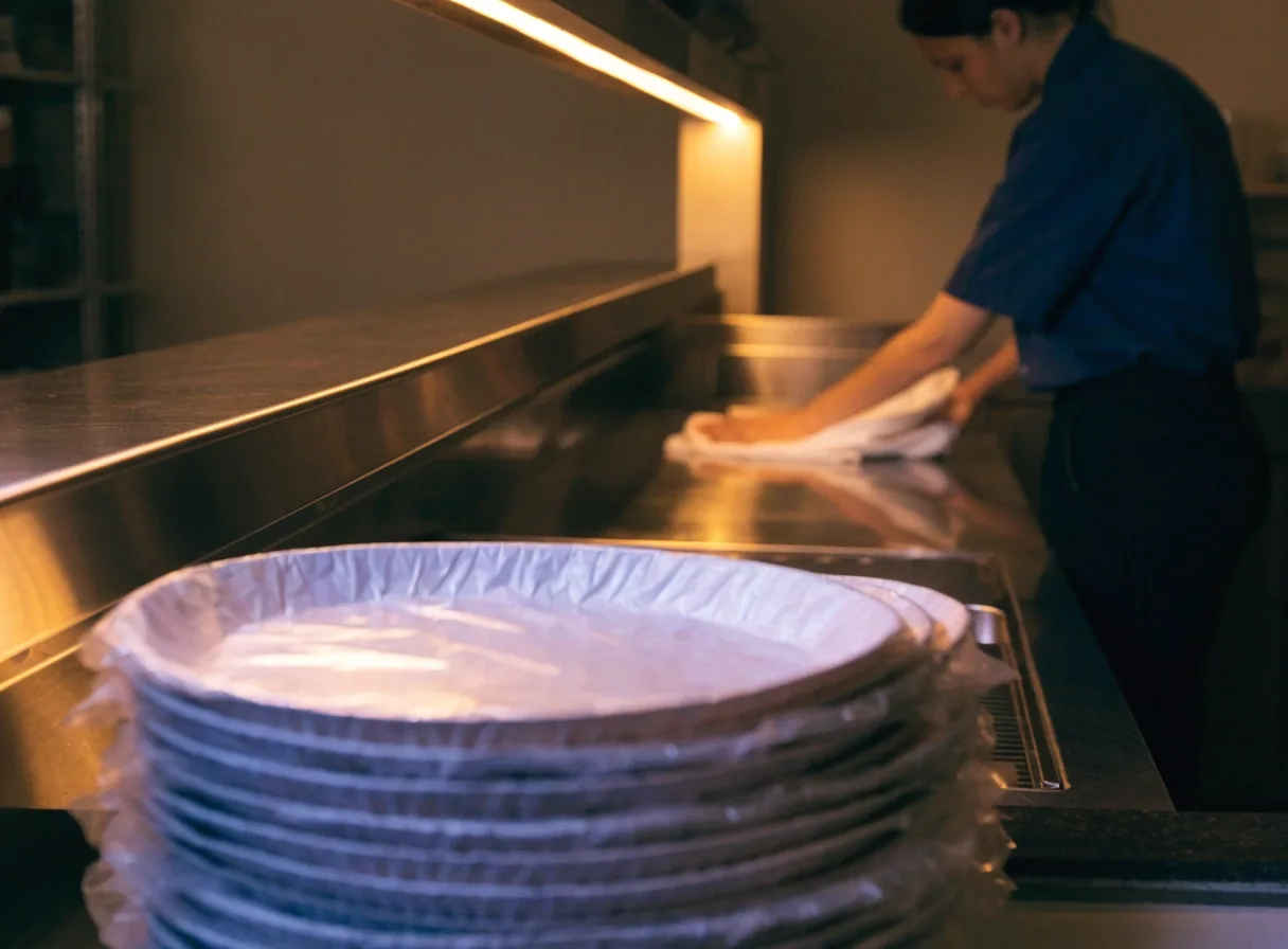 A counter worker wiping down trays at a doughnut shop counter near closing time